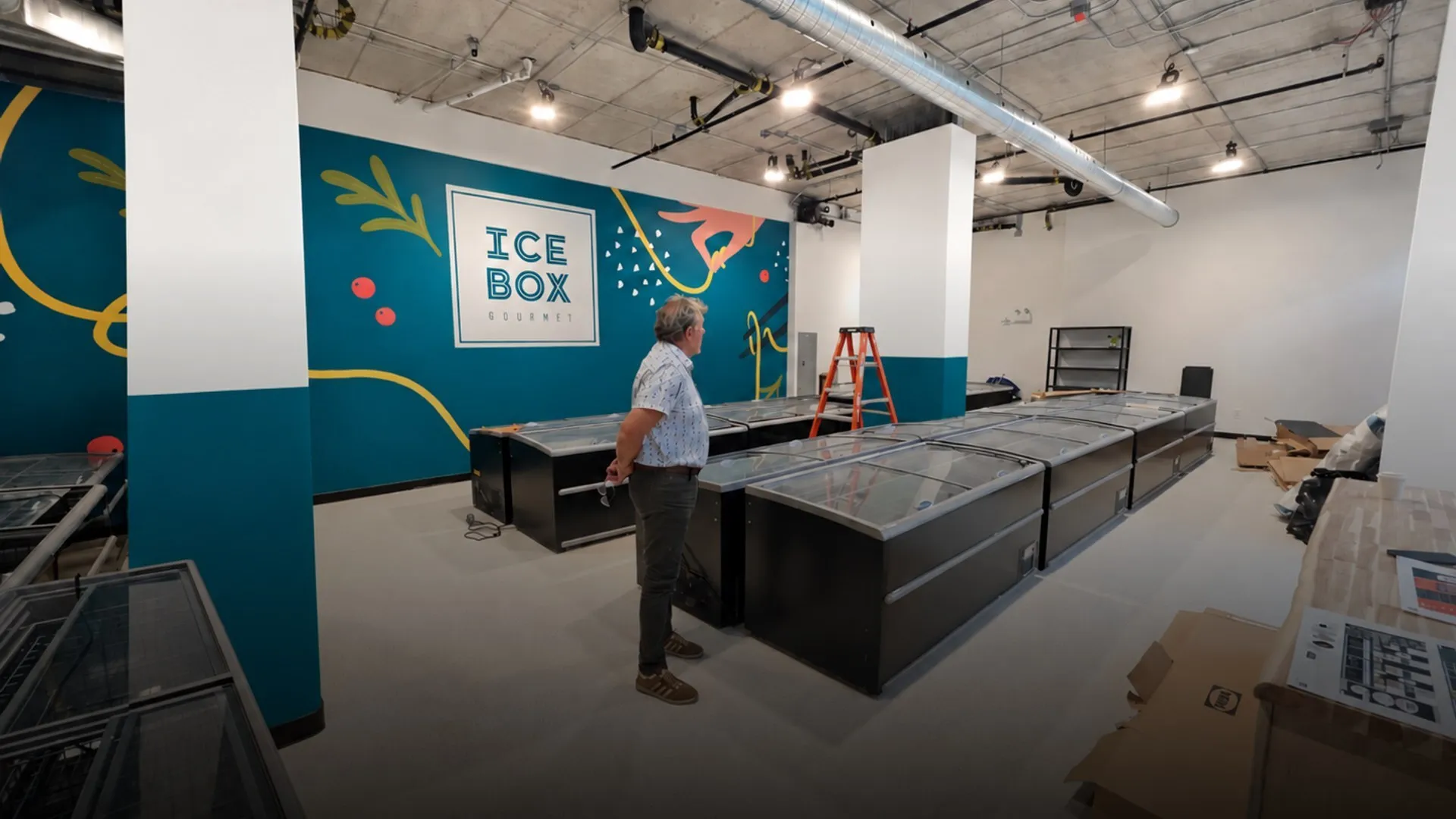 Inside the ICEBOX Gourmet boutique, with the teal brand mural and freezers being installed